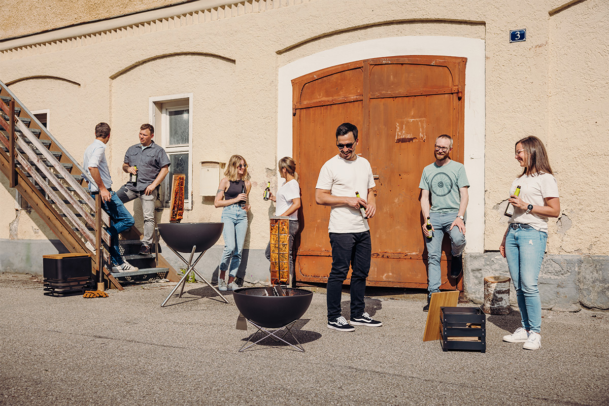 Hier ist eine Gruppe von Menschen um einen Feuerplatz herum abgebildet, mit dem Flame-grilled Lachs-Brett.
