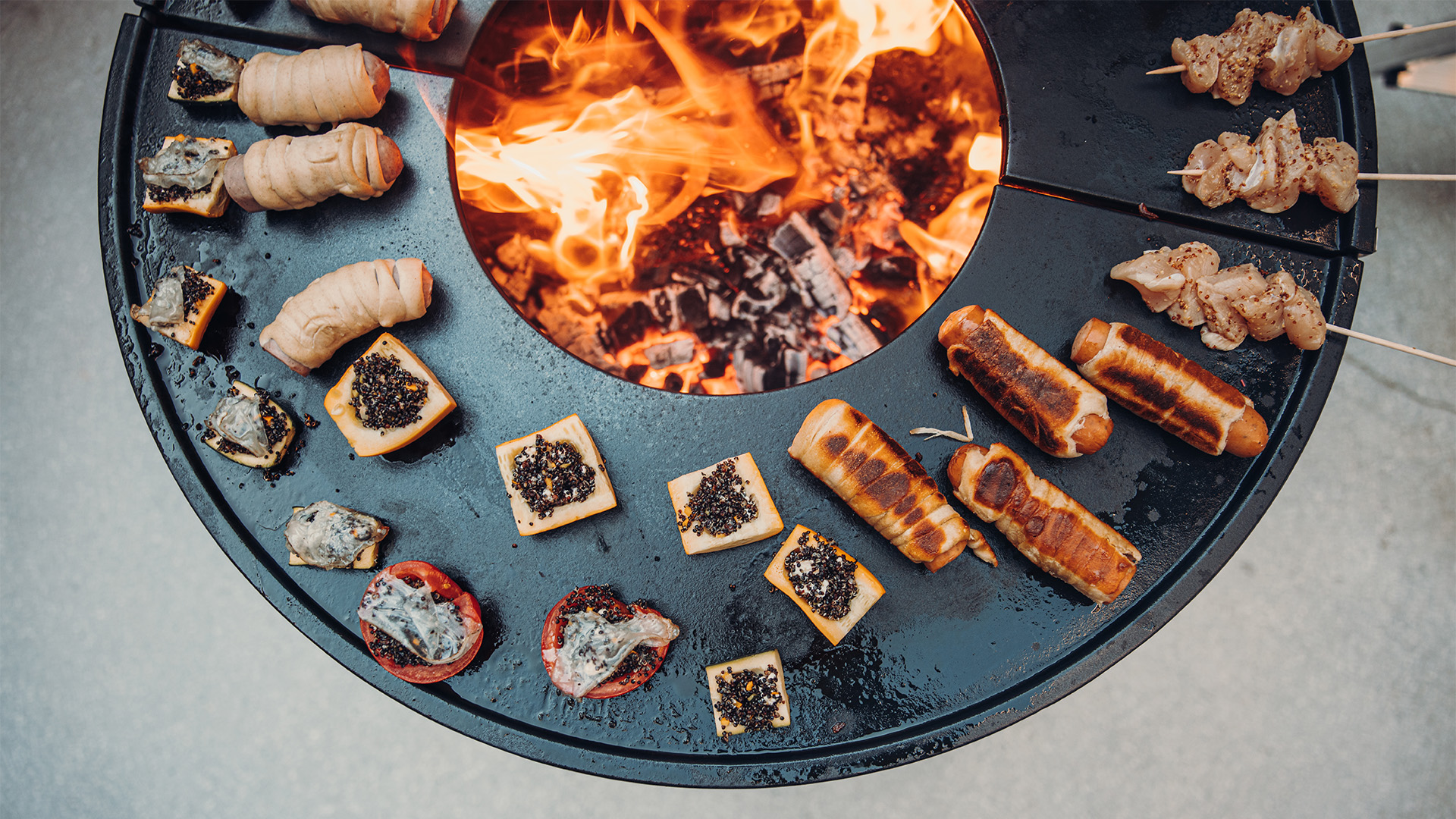 Das Foto zeigt einen Feuerplatz mit einer Menge Essen darauf, mit dem BOWL 70 Plancha BBQ Set niedrig.