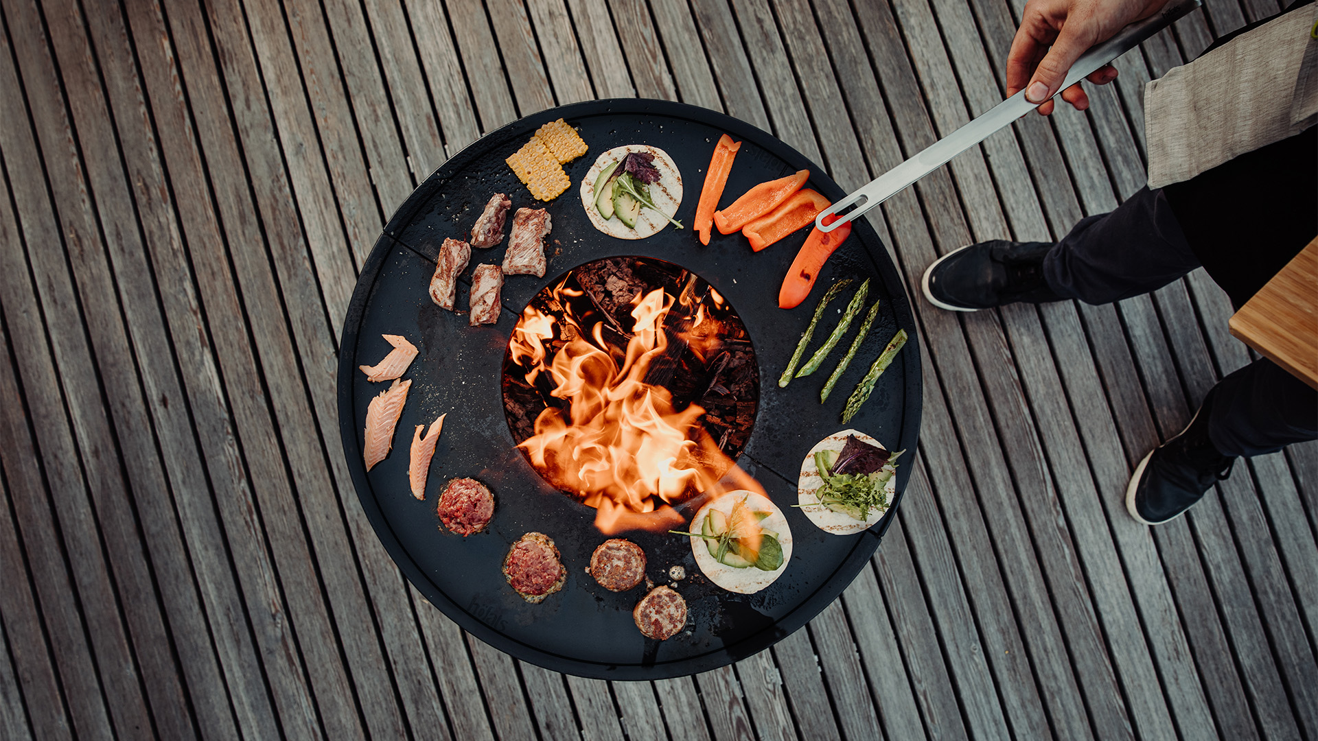 An inviting scene with a person is cooking food on a grill, highlighted by the presence of the 00256 Bowl 57 Plancha .