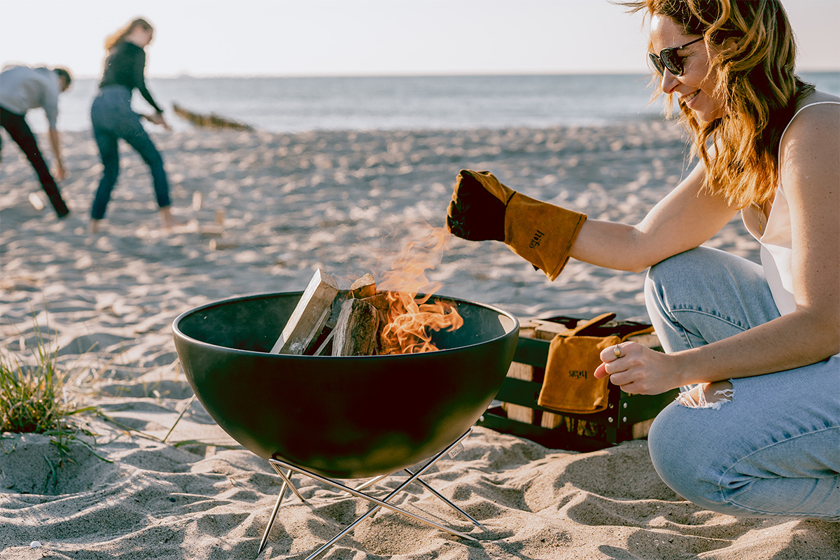 BOWL 57 Bol à feu avec pied en étoile Une représentation d'une femme assise sur la plage, mettant en vedette le BOWL 57 avec son socle étoilé comme élément central et fonctionnel.