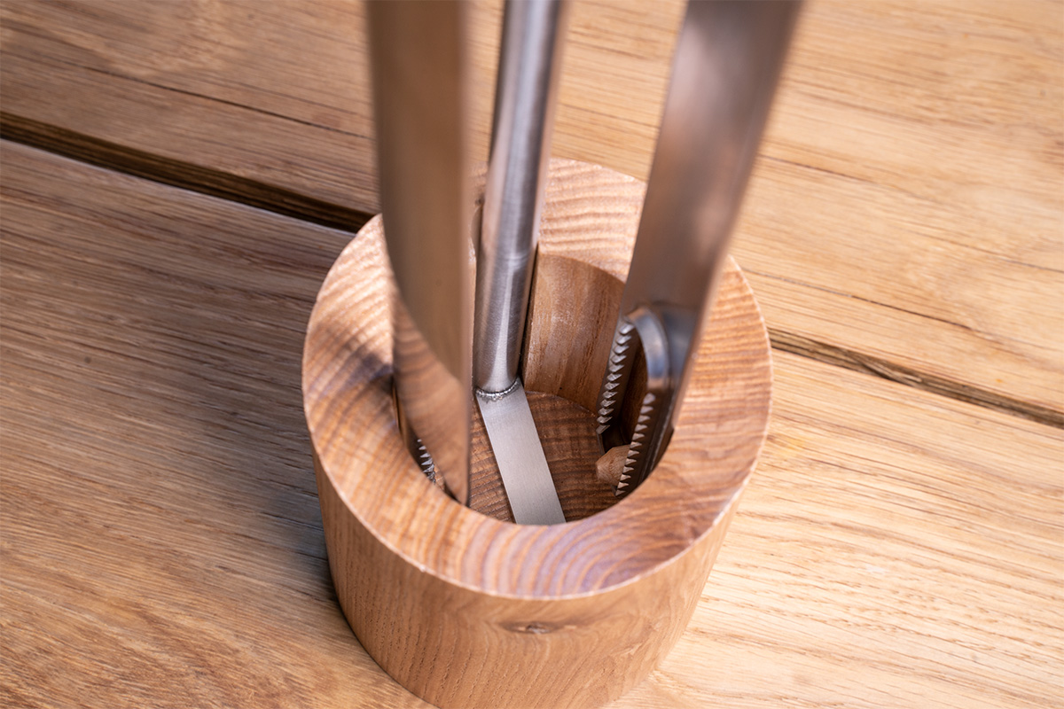 Fire Tools Set 3 pcs A tong in a wooden holder on a table, enriched by the presence of the 00251 Fire Tools Set 3 pcs, which merges design with utility.