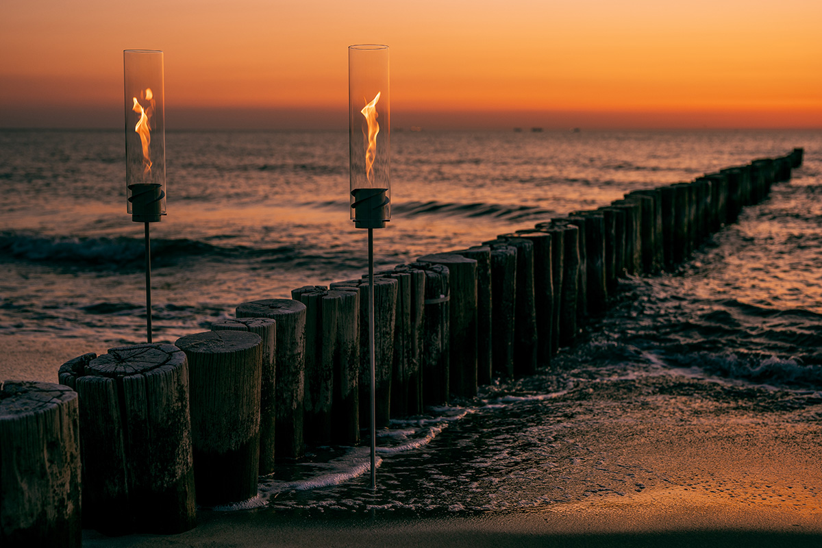 A depiction of a wooden fence on a beach at sunset, featuring the Spin Ground Spike silver as a central and purposeful element.