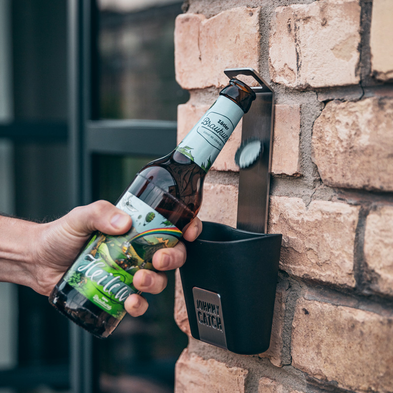 Une vue d'une personne tenant une bouteille de bière dans un mur, avec la coupe JOHNNY CATCH.