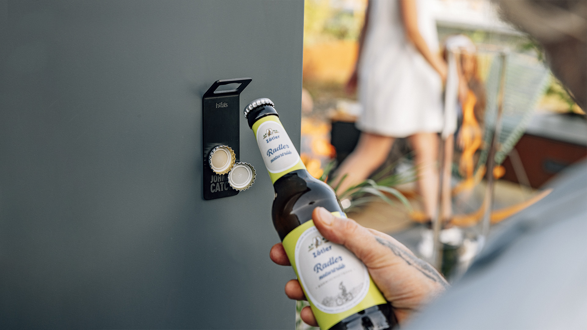 Scene showing a person holding a bottle of beer in their hand, where the 00841 Johnny Catch Magnet Black Bottleopener stands out for its practical elegance.