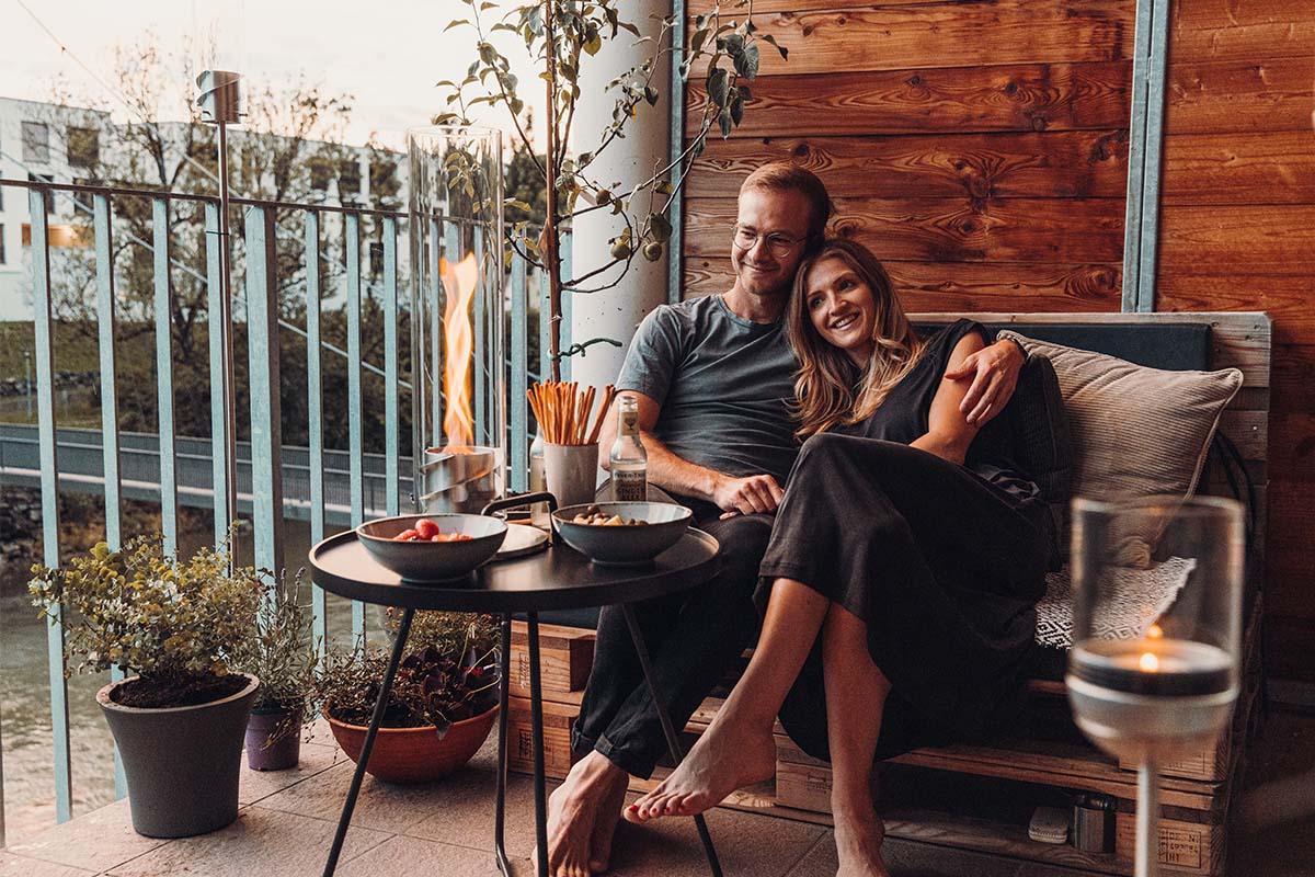 SPIN 120 Tischfeuer silber Szene, in der ein Mann und eine Frau auf einem Sofa sitzen und eine Platte Essen vor sich haben, wobei der Spin 90 Tischfeuer in Silber durch seine praktische Eleganz hervorsticht.