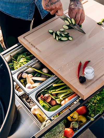 Un homme est représenté en train de couper des légumes, avec la FIRE KITCHEN.