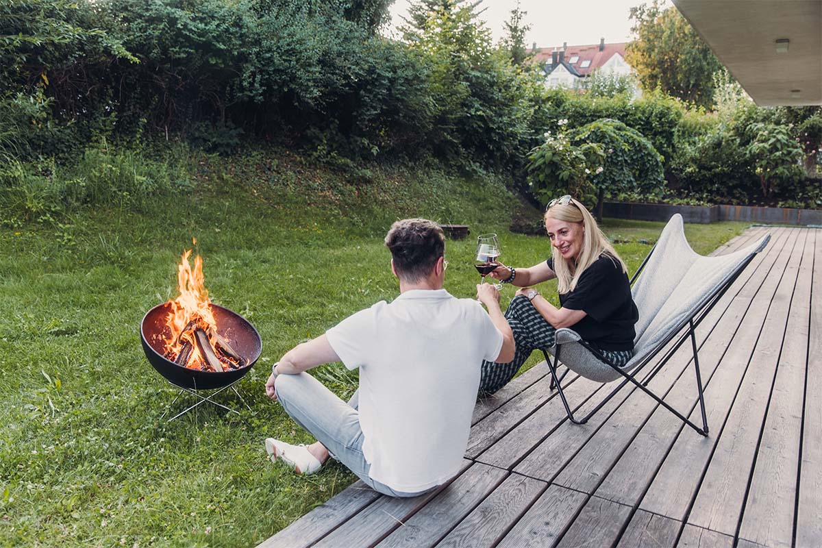 BOWL 57 Sternfuß Eine einladende Szene mit einem Mann und einer Frau, die auf einer Bank neben einem Feuerkorb sitzen, hervorgehoben durch die Präsenz des 00343 Bowl 57 Sternfuß.