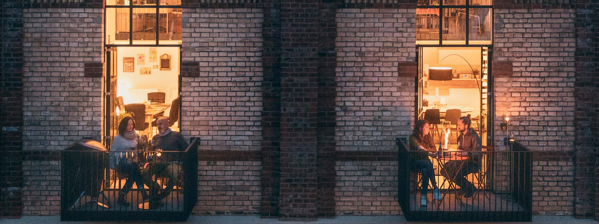 Das Foto zeigt Menschen, die nachts auf dem Balkon eines Gebäudes sitzen, mit dem LOGO SPIN Tischkamin.