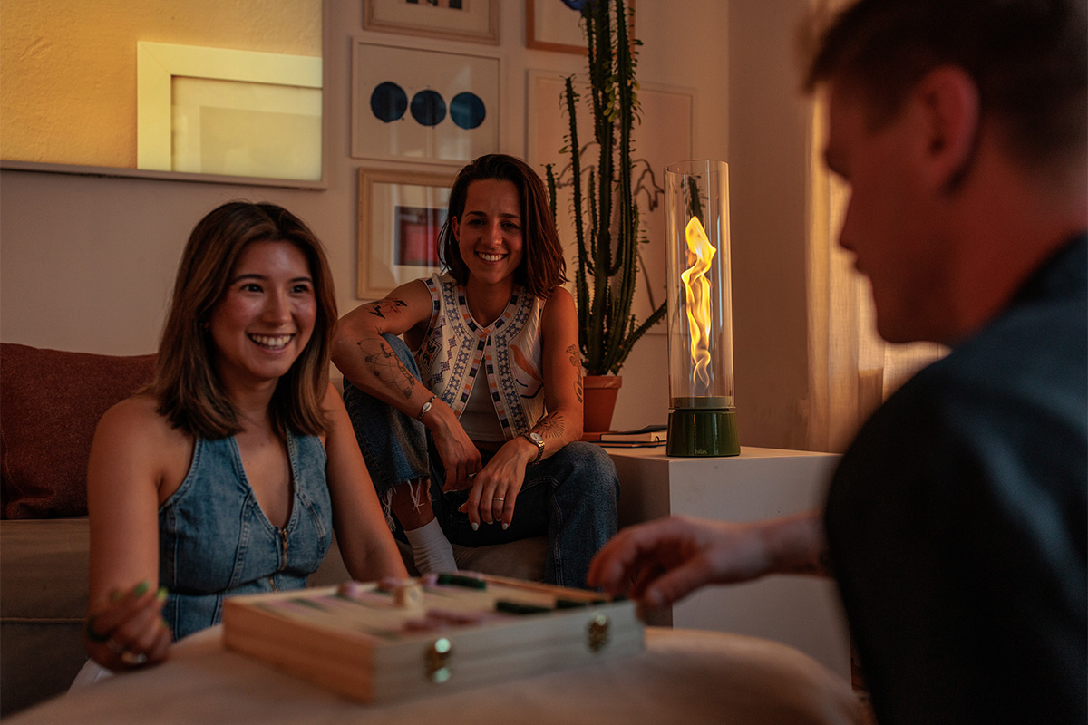 SPIN air 1200 Tabletop Fireplace enamel green The Spin Air 1200 Tablefire Emaille Green adds cozy charm to the room where a woman lounges on a sofa.