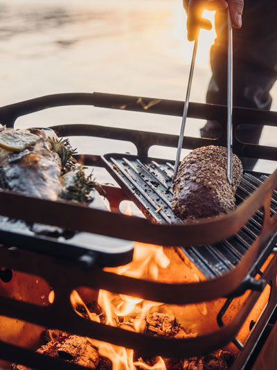 Un homme Grille de la viande sur un gril, le CUBE brasero avec Plancha complète le moment avec son design réfléchi.