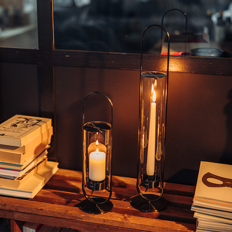 La OVAL CANDLE est présentée comme une table avec une bougie et des livres dessus, créant une image élégante et accessible.