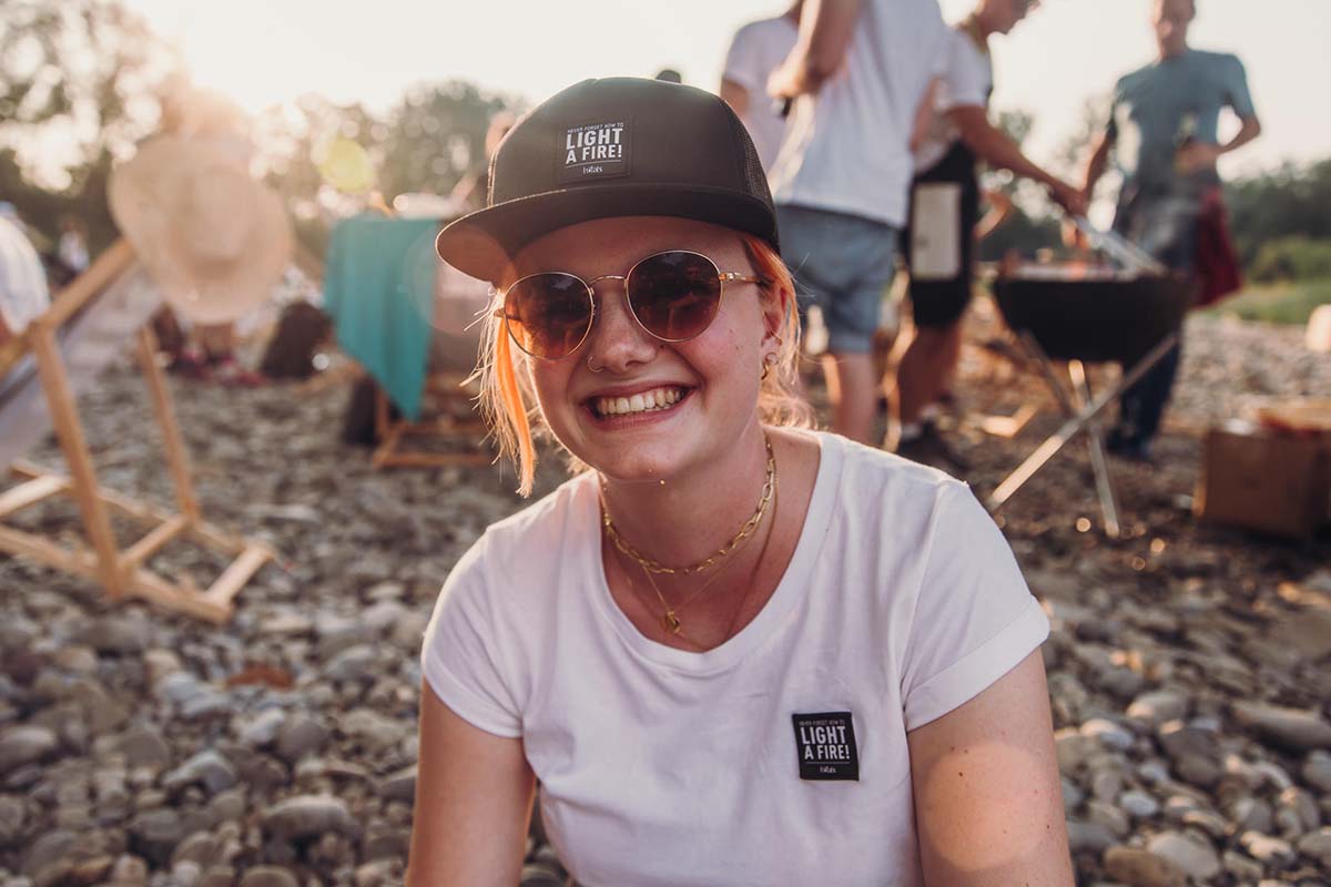 CASQUETTE noir Une femme portant un chapeau et des lunettes de soleil est assise sur des rochers.