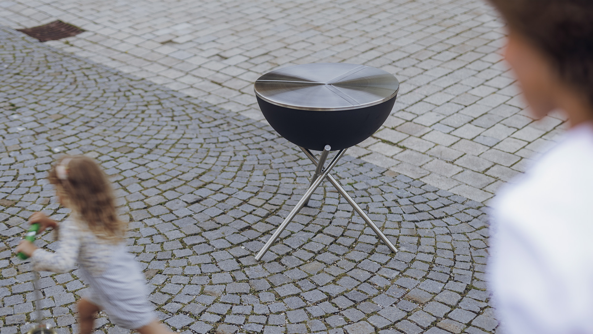 Ein Bild von einem kleinen Mädchen, das auf einen Grill zuläuft, mit dem 00479 Bowl 70 Deckel als zentralem und zweckmäßigem Element.