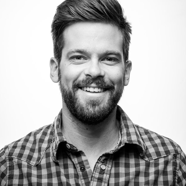 Un homme barbu souriant à la caméra.