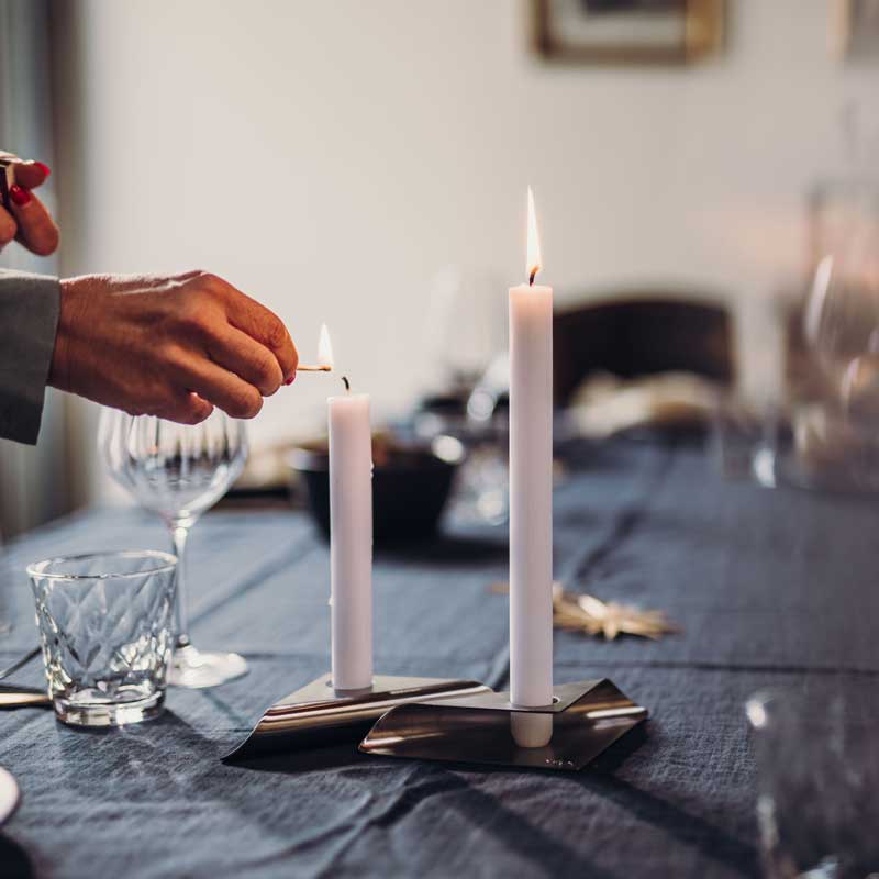 Experience a man lighting a candle at a table with the refined touch of the Square Candle Candleholder