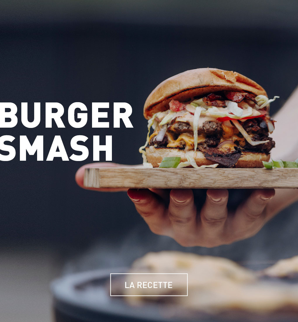 Une personne tient un sandwich hamburger dans sa main.