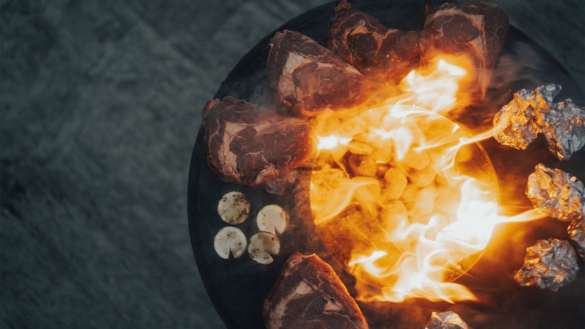 Ici est représenté un brasero avec beaucoup de viande dessus, avec le BOWL 57 Plancha BBQ Set bas.