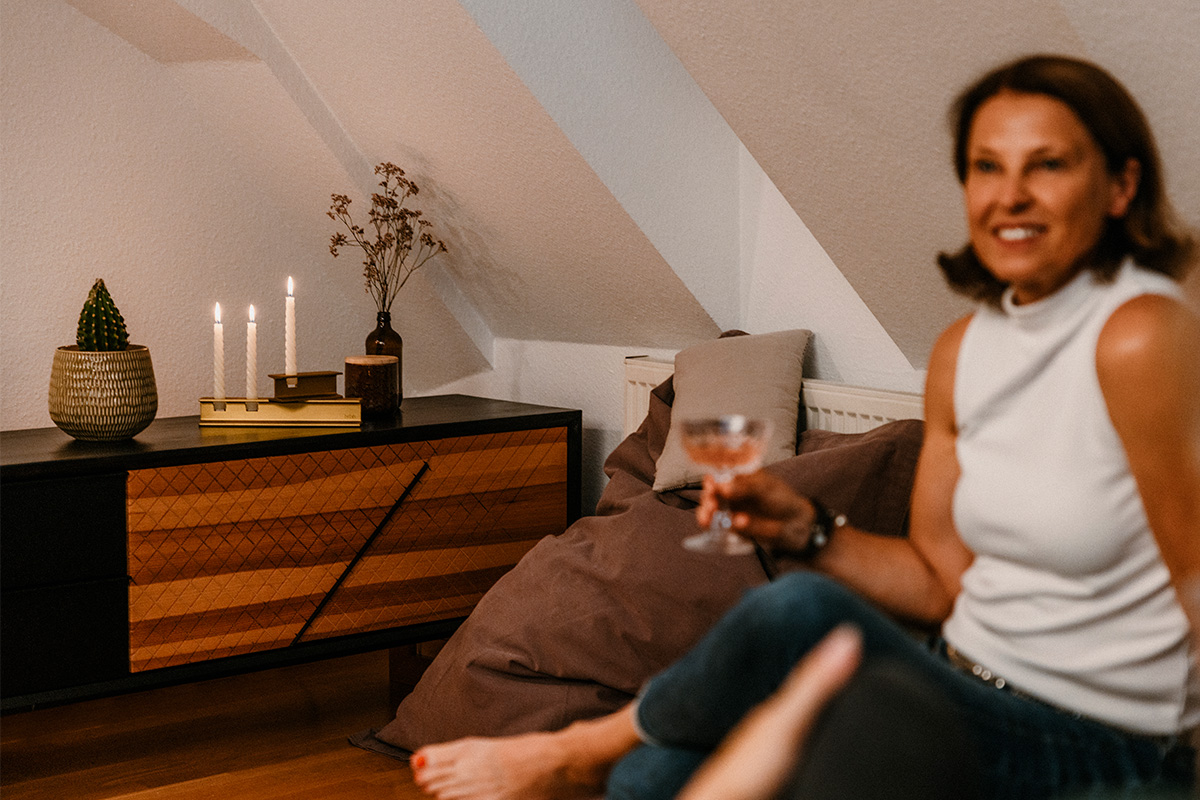 HENRY METAL I Candleholder gold Scene showing a woman sitting on a couch holding a glass of wine, where the 00662 Henry Metal II Gold stands out for its practical elegance.