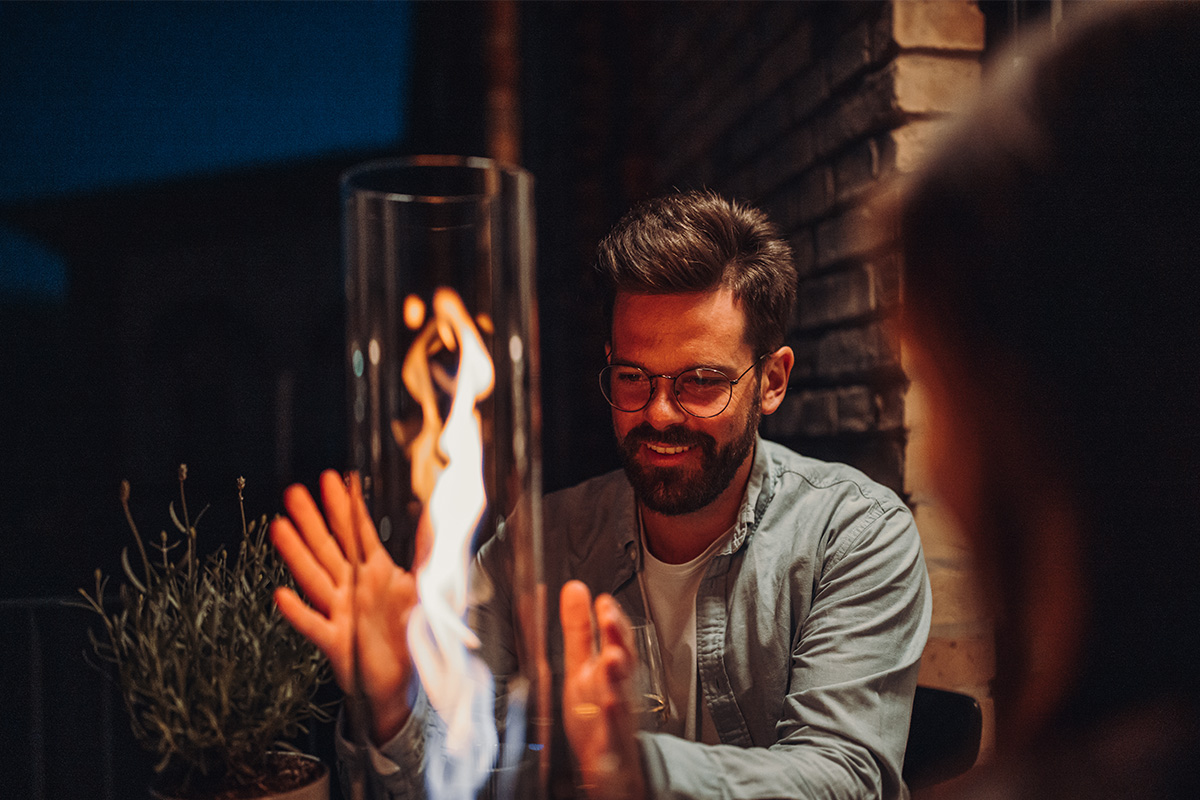 SPIN 120 Tischfeuer silber Ein Bild zeigt einen lächelnden Mann, der ein Feuer betrachtet, wobei der Spin 90 Tischfeuer in Silber als zentrales und zweckmäßiges Element dient.