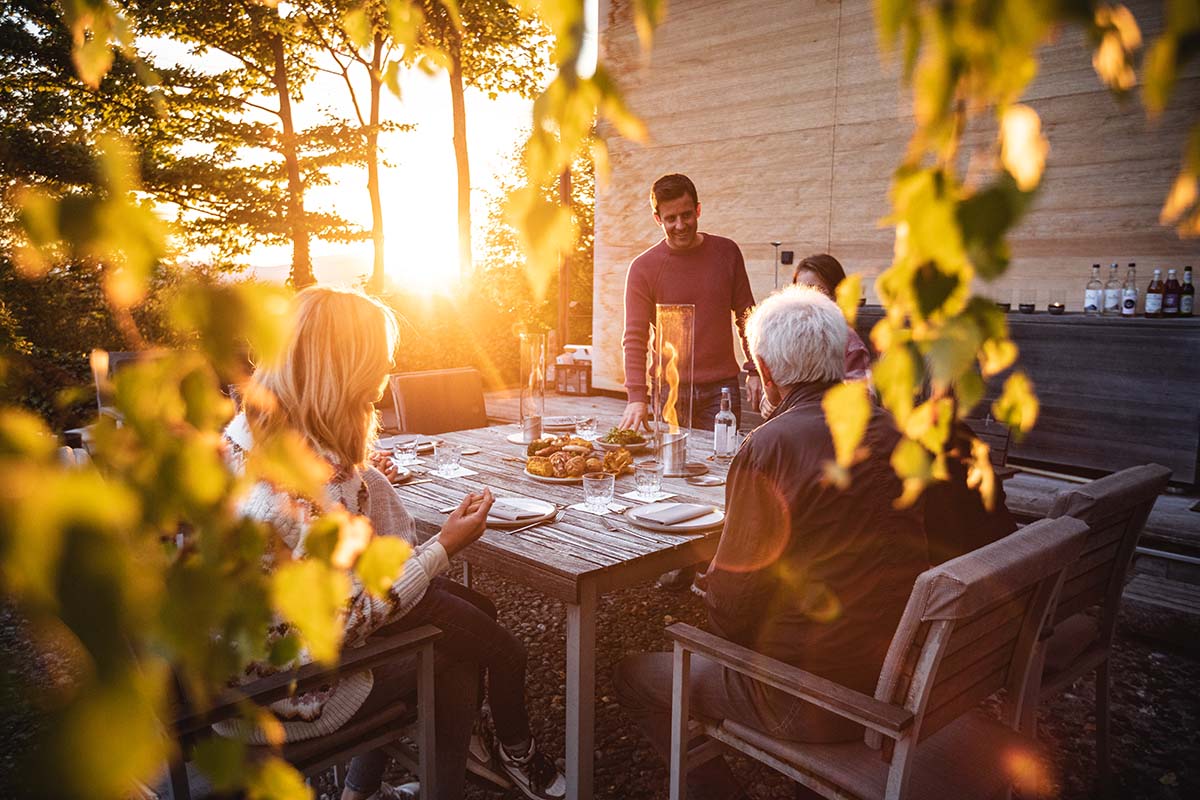 SPIN 120 Tischfeuer silber Szene, in der eine Gruppe von Menschen um einen Tisch sitzt, wobei der Spin 90 Tischfeuer in Silber durch seine praktische Eleganz hervorsticht.