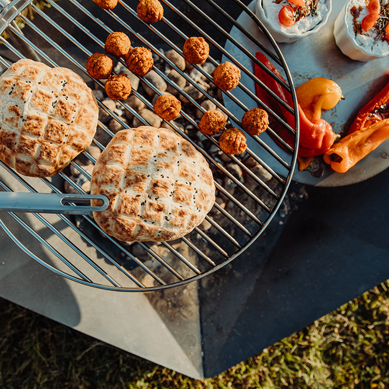 Szene zeigt einen Grill mit Essen darauf, wobei der Triple Kamin durch seine praktische Eleganz hervorsticht.