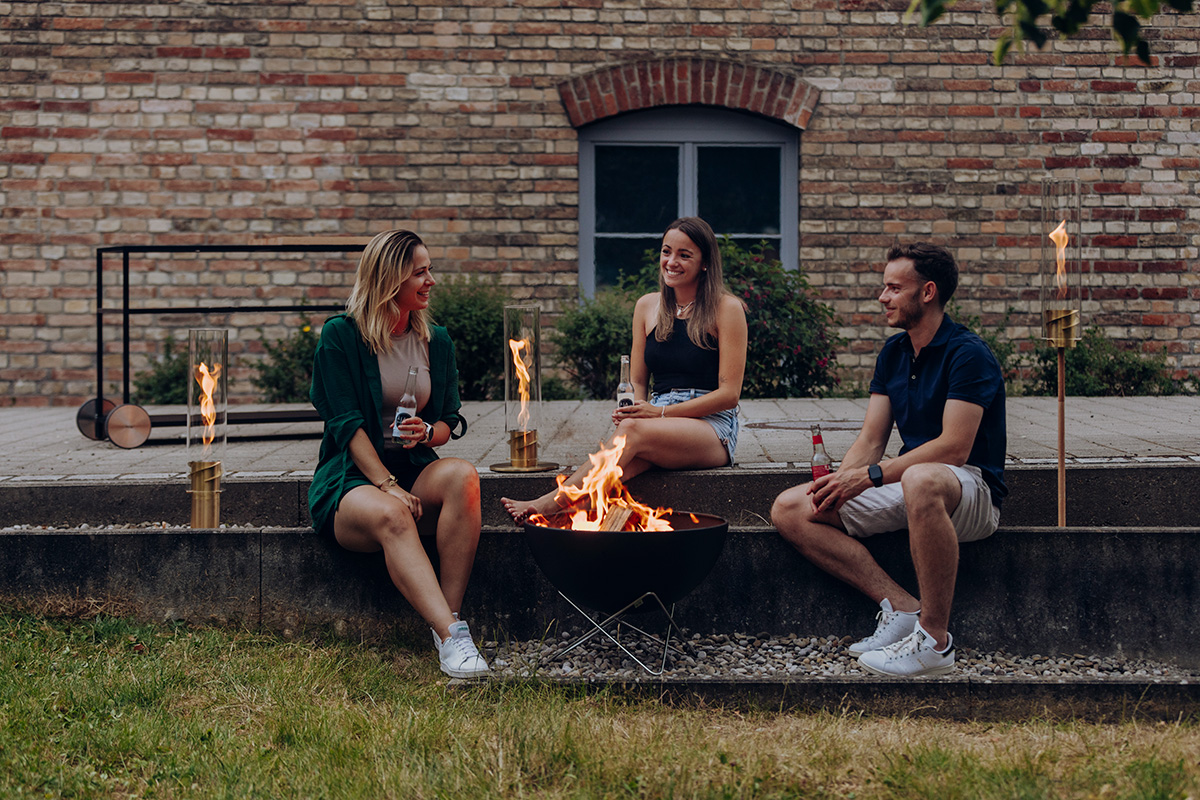 SPIN classic 1200 Cheminée de Table or La photo présente un homme et une femme assis sur un banc avec un feu, avec la cheminée de table SPIN 1200 en or.