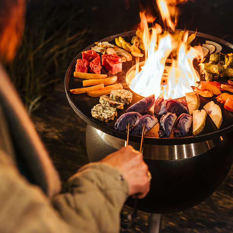 A depiction of a person is cooking food on a fire, featuring the Moon 45 as a central and purposeful element.
