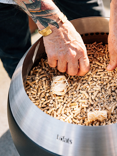 Une personne met des copeaux de bois dans un brasero. Montrant comment allumer le MOON 45.