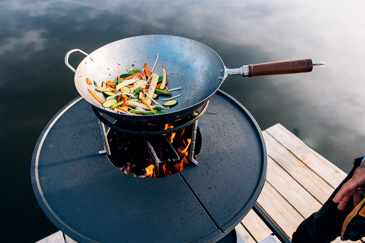 Hier ist eine Person abgebildet, die Essen auf einem Grill auf einem Steg zubereitet, mit dem BOWL 70 Sear Grate.