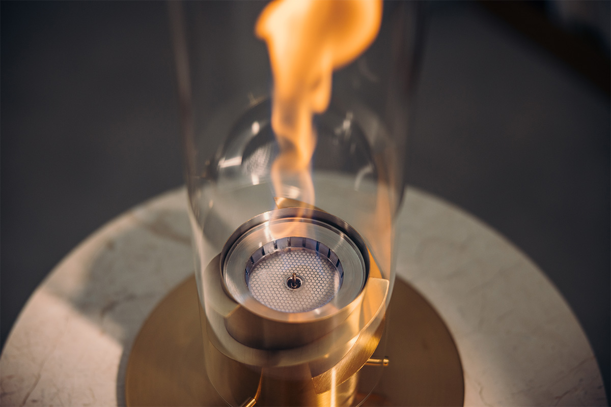 SPIN 900 Tischfeuer gold Der 00699 Spin 1200 Tischfeuer Gold wird als Glaszylinder mit einer Flamme im Inneren dargestellt, was ein stilvolles und zugängliches Bild ergibt.
