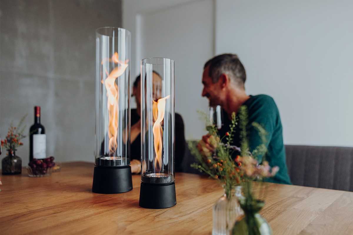 SPIN air 900 Tischfeuer mattschwarz SPIN air 1200 und 900 mattschwarz auf einem Küchentisch mit zwei Personen welche mit einem Rotwein anstoßen und sich unterhalten
