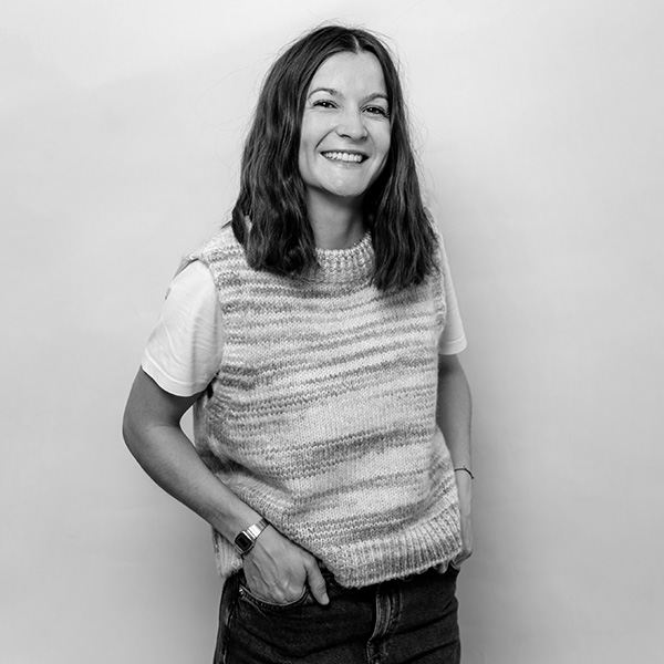 Une femme en pull et en jeans debout contre un mur.