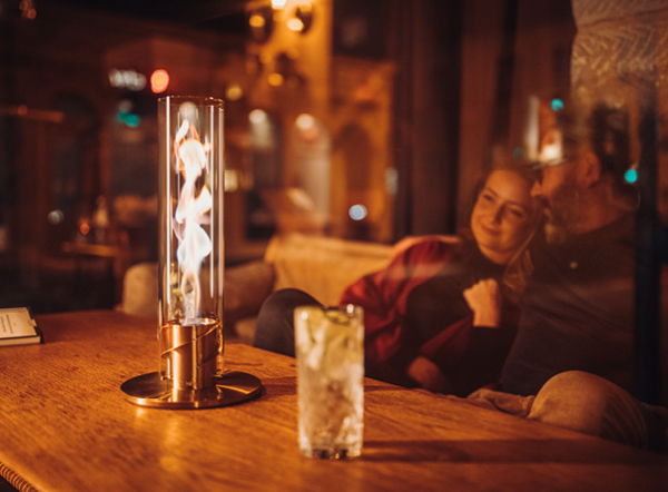 Ein Mann sitzt mit einer Frau an einem Tisch und genießt die Wärme des SPIN Tischfeuer.