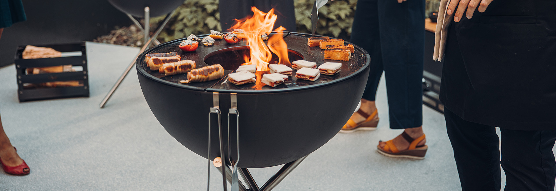 This image shows a man and woman standing next to a fire pit, with the BOWL 57 Plancha.