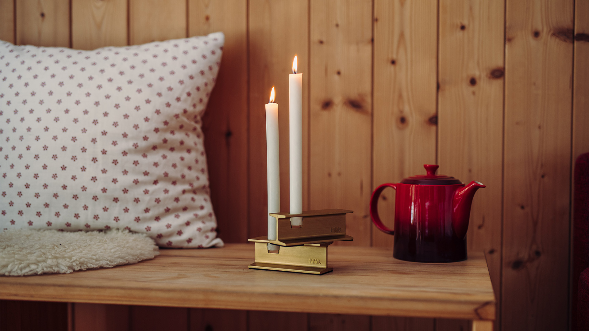 Illustrated is a candle and a red mug on a table, with the HENRY METAL I Candleholder gold.