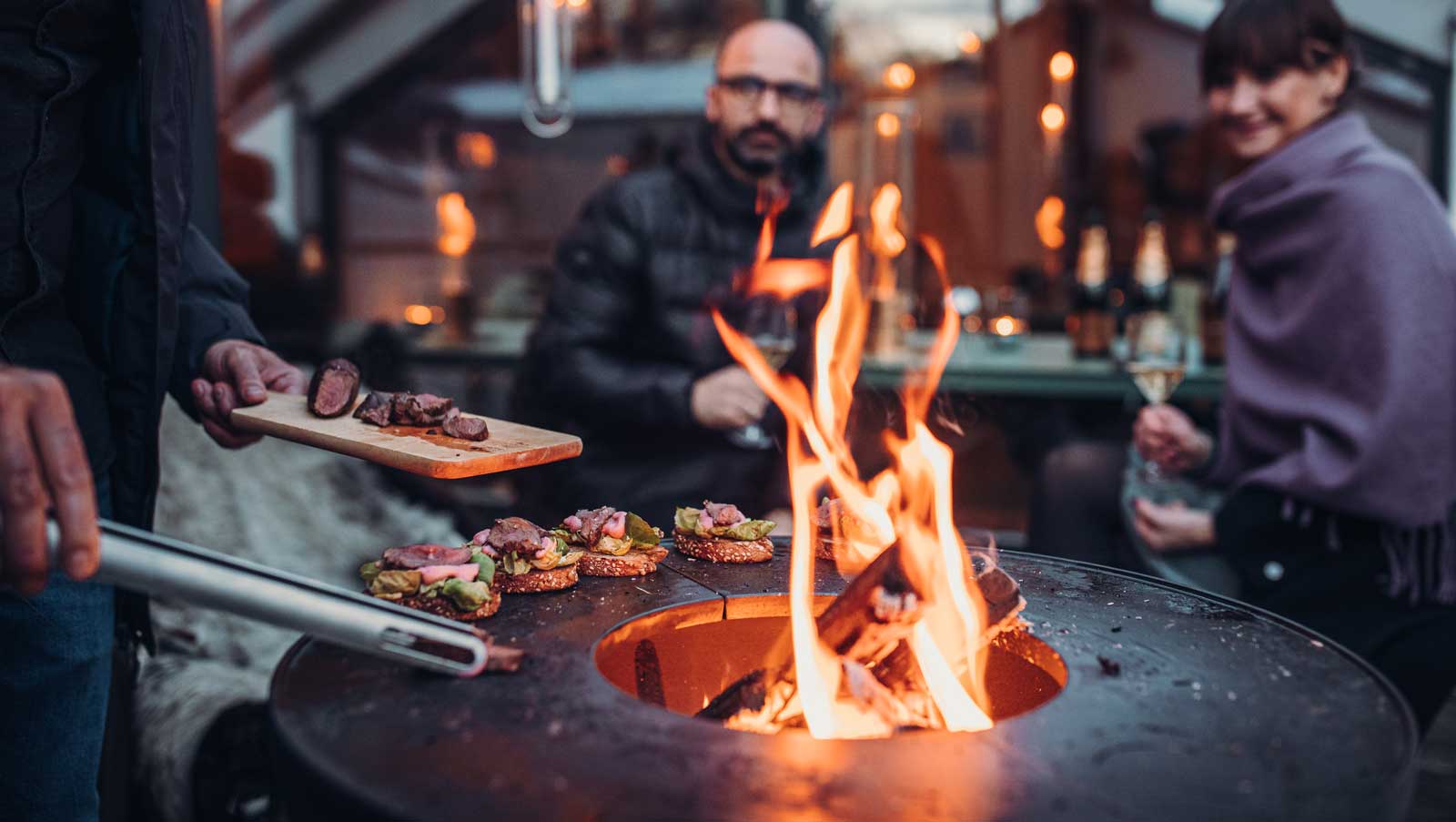 A view of a man is cooking food on a grill, with the BOWL Fire Bowl.