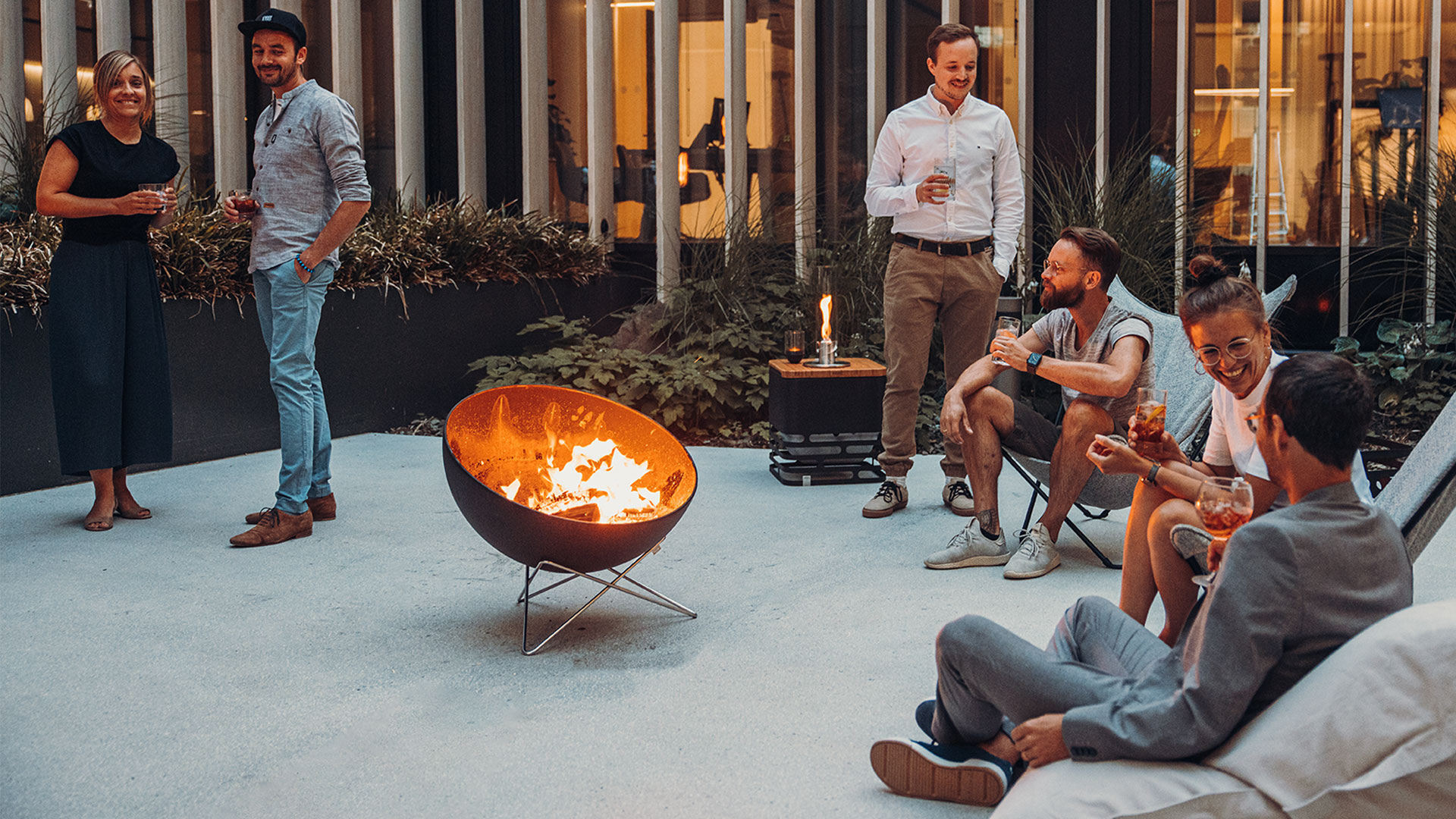 Experience a group of people sitting around a fire pit with the refined touch of the 00257 Bowl 70 with starstand .
