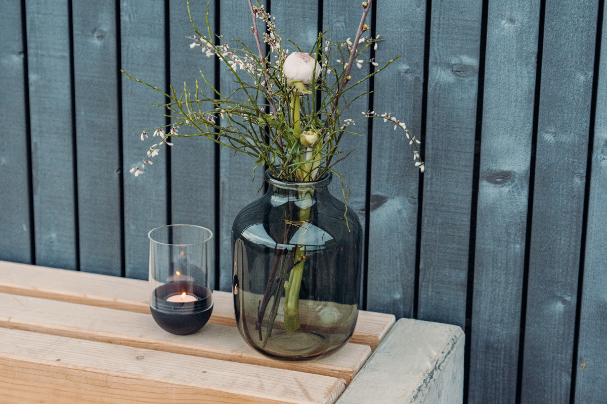 The 00544 Gravity Candle black integrates seamlessly into the setting, where a vase with flowers and a candle on a wooden table.
