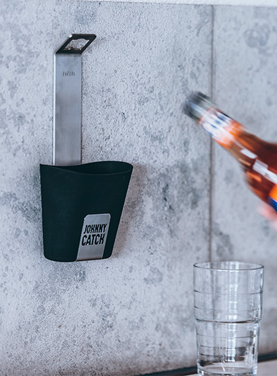 Une bouteille d'alcool est versée dans un verre, enrichie par la présence du décapsuleur Johnny Catch Cup, qui allie design et utilité.