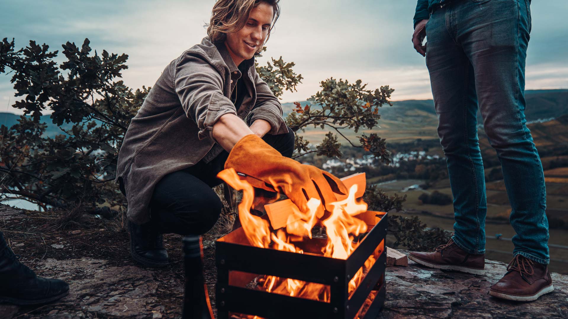 Eine Frau sitzt auf einem Felsen am Feuer, bereichert durch die Präsenz der Glove Tools, die Design mit Nützlichkeit verbinden.
