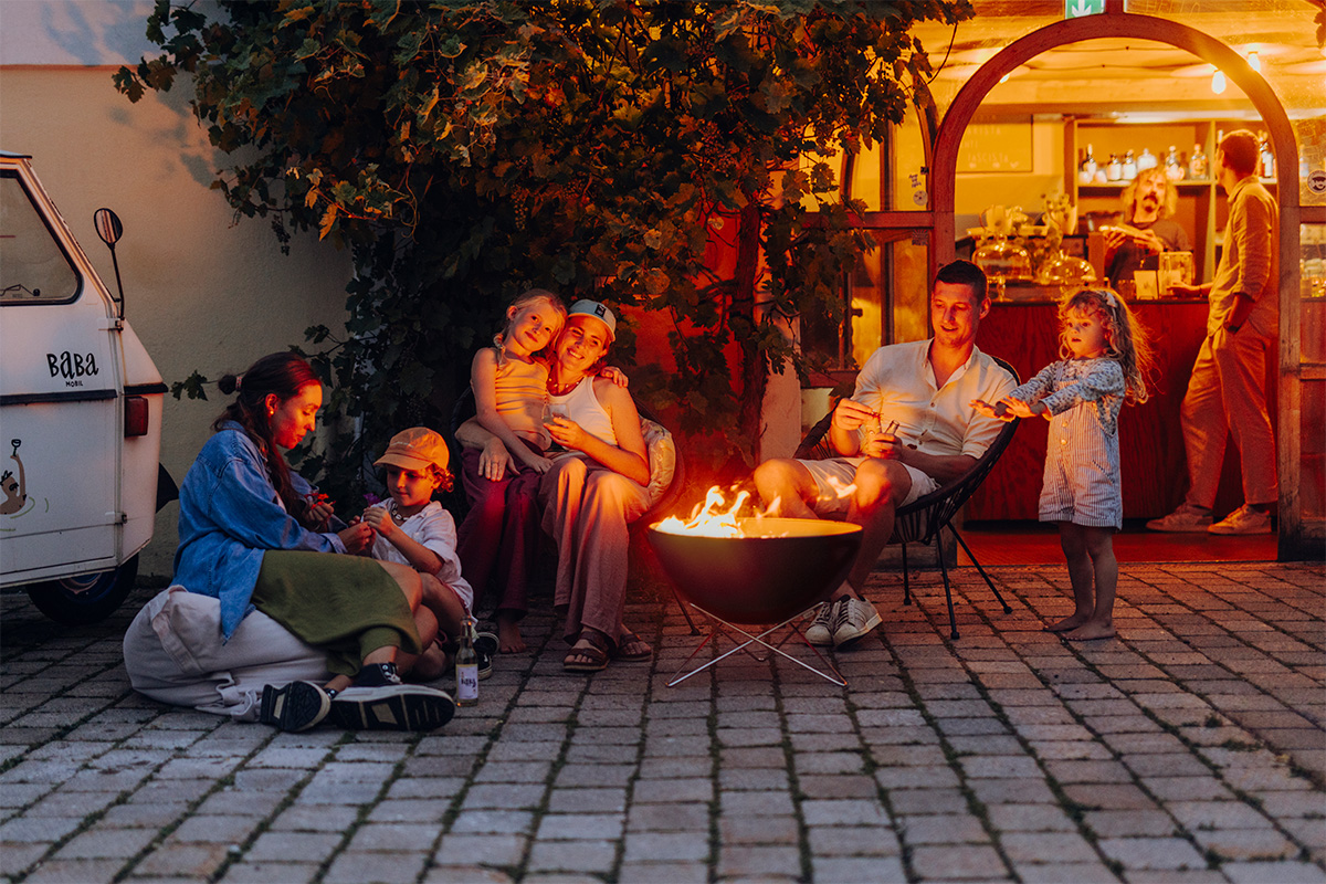Scène montrant un groupe de personnes assises autour d'un brasero, où le BOWL 57 avec son support en étoile se distingue par son élégance pratique.