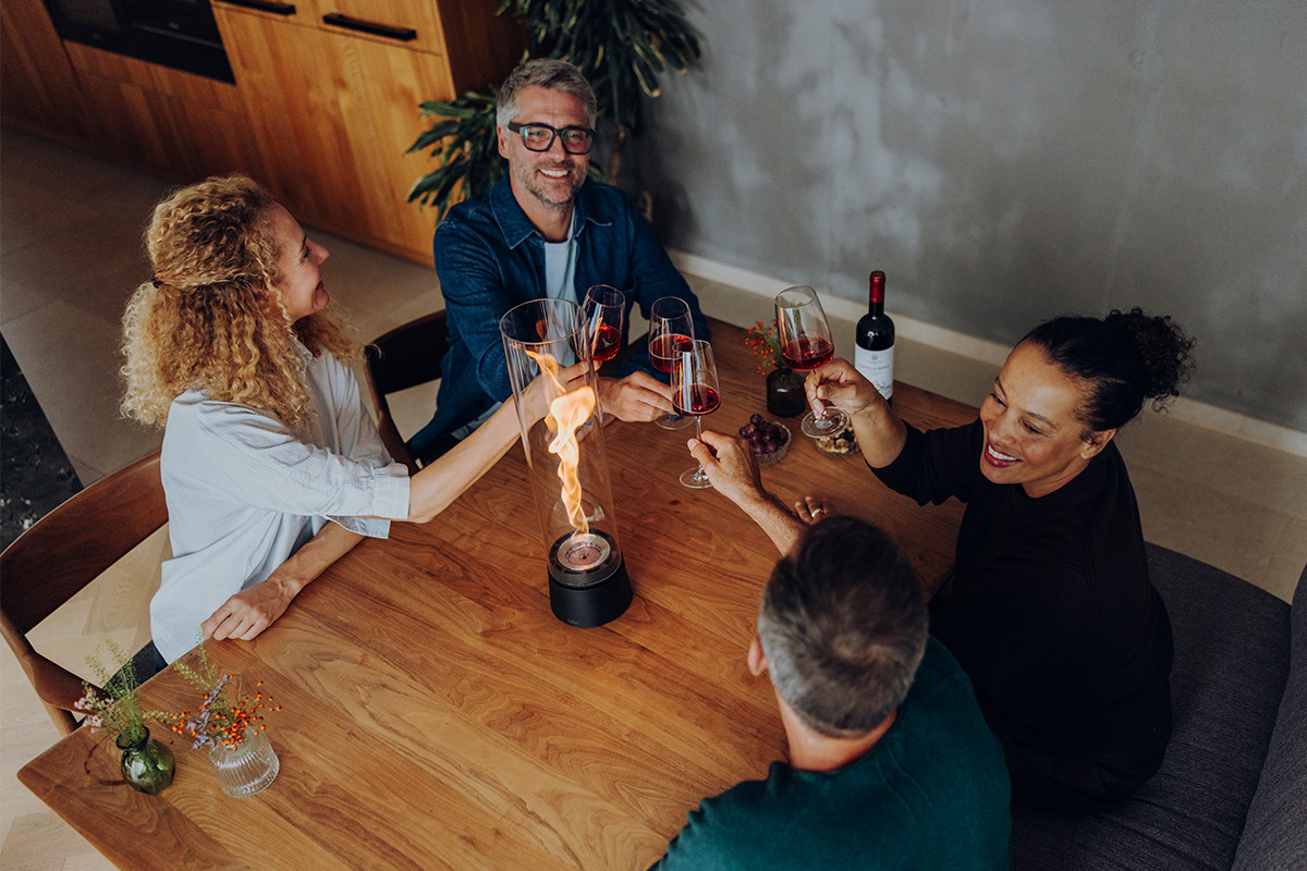 SPIN air 1200 Feu de table noir mat SPIN air 1200 und 900 mattschwarz auf einem Küchentisch mit vier Personen welche mit einem Rotwein anstoßen