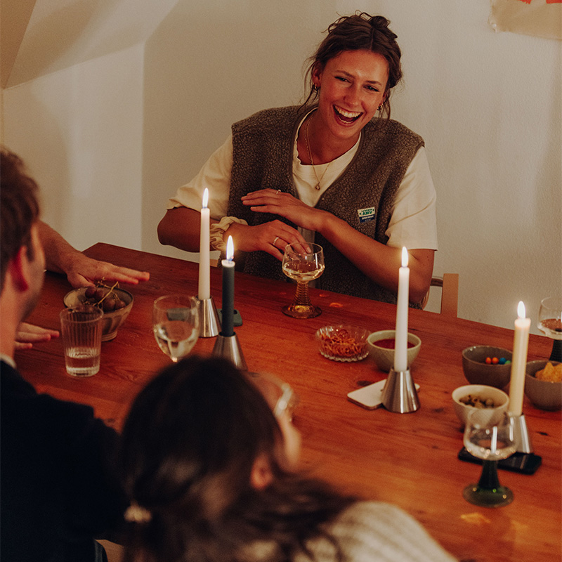 Drei Digi Detox mit brennender Kerze auf Esstisch, an dem drei Personen sitzen.