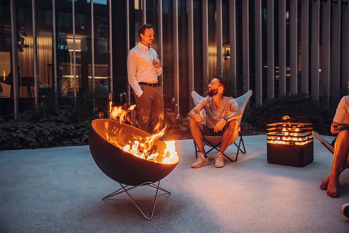 BOWL 70 Sternfuß Die 00259 Bowl 70 Sternfuß fügt sich nahtlos in die Umgebung ein, in der eine Gruppe von Menschen um einen Feuerplatz sitzt.