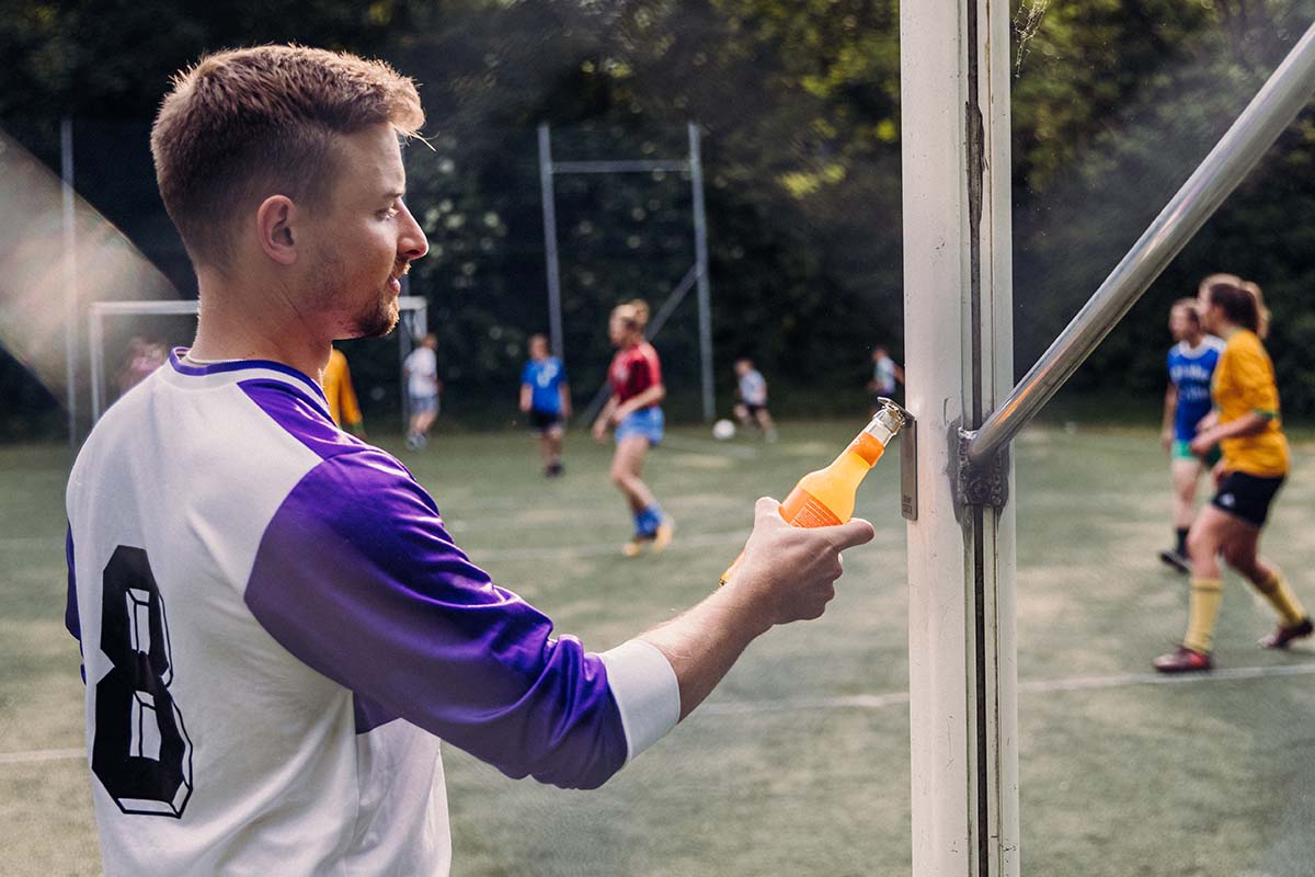 JOHNNY CATCH Aimant Décapsuleur argent Un homme tient une boisson à l'orange et ouvre la bouteille. L'ouvre-bouteille magnétique Johnny Catch complète le moment avec son design réfléchi.